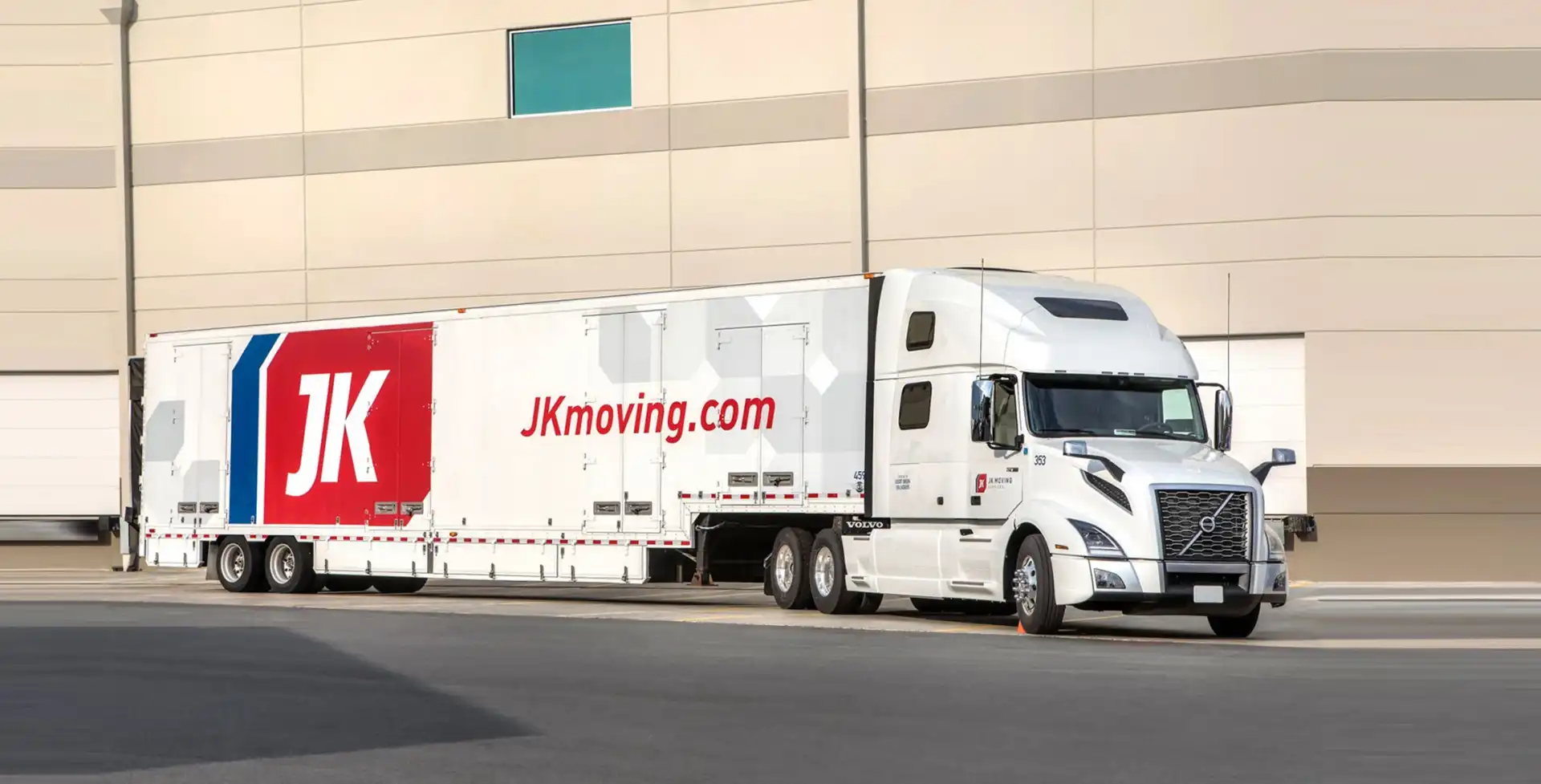 White JK Moving Services semi-truck with branded trailer parked outside a warehouse facility.