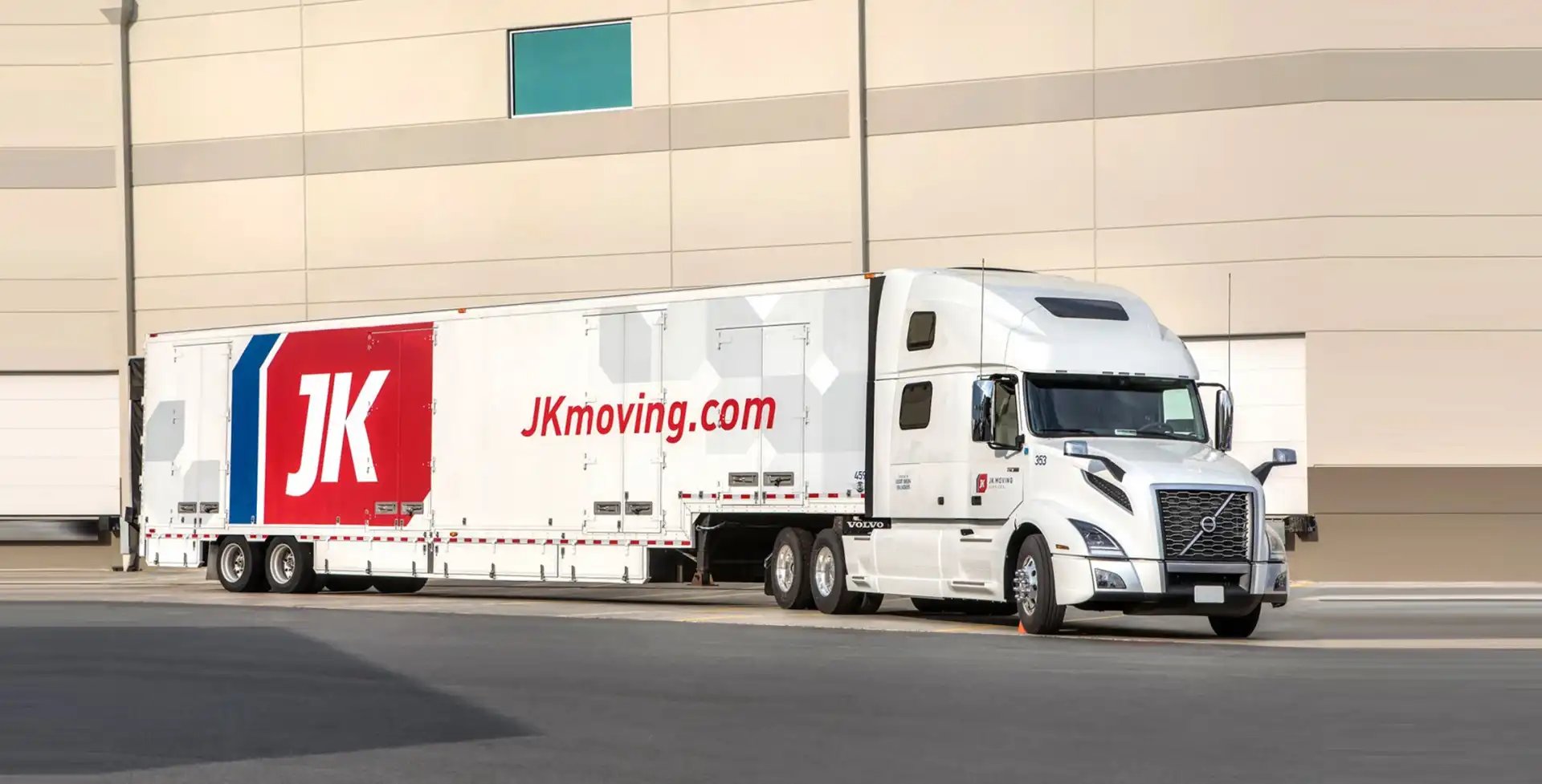 White JK Moving Services semi-truck with branded trailer parked outside a warehouse facility.